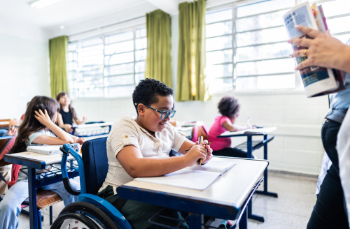 Boy with glasses in a wheelchair in class with fellow students