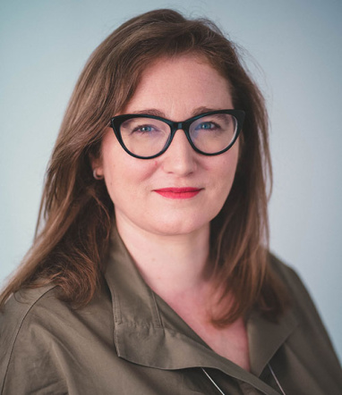 Portrait photo of Caroline smiling at the camera, wearing glasses
