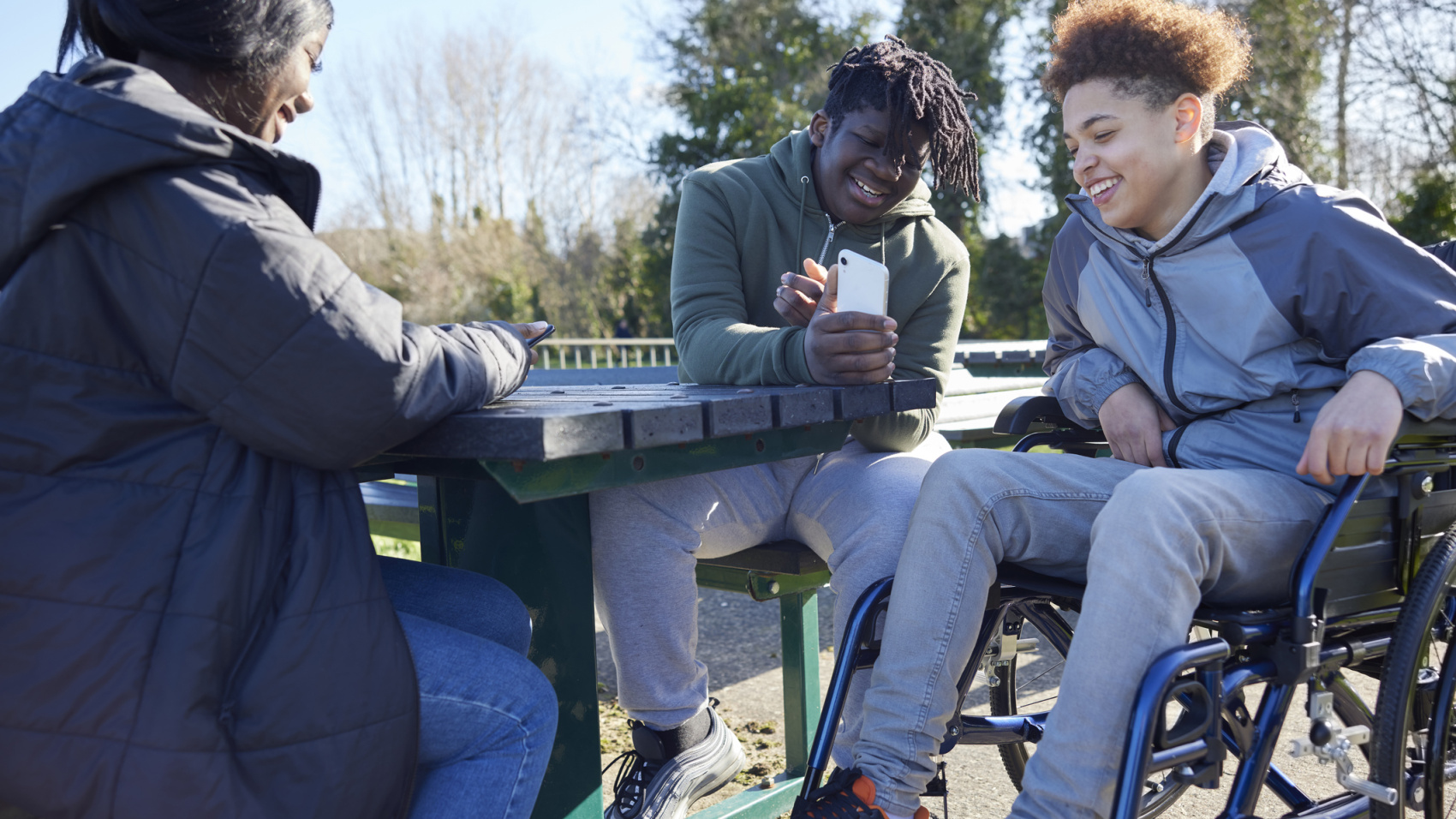 Teenage girl in wheelchair laughing with two friends outside 