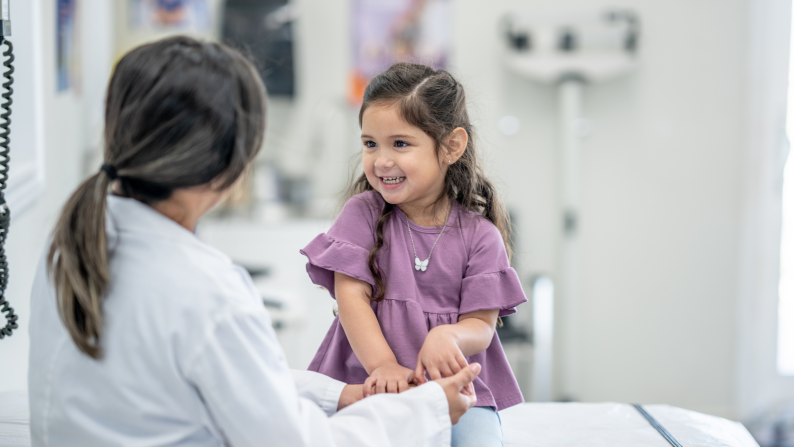 Young girl smiles at and sits opposite healthcare professional in what looks like a GP or hospital room